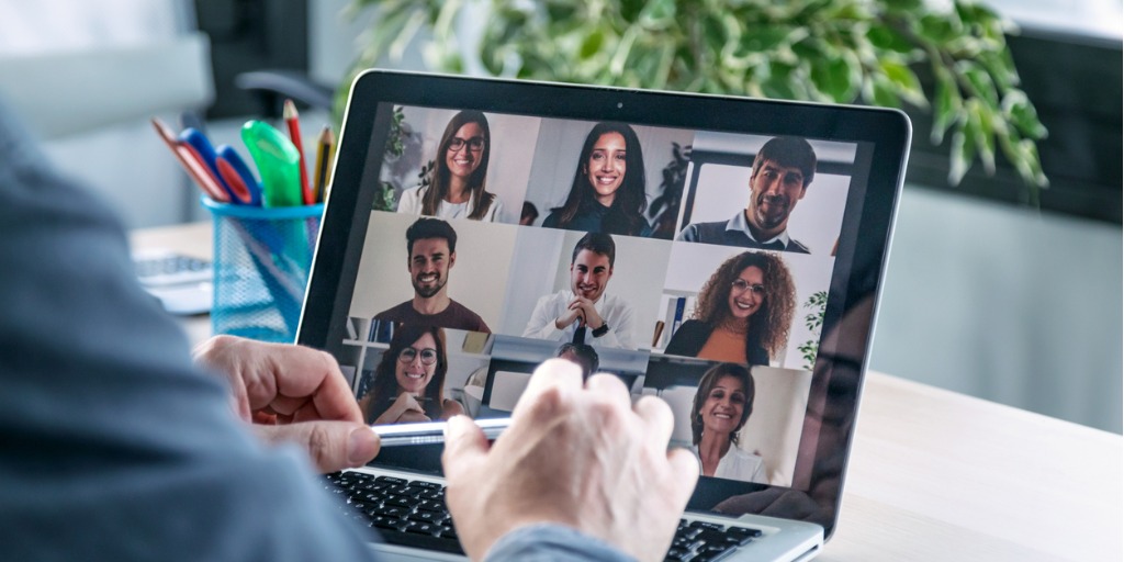 A group of diverse business colleagues participate in a virtual staff meeting during the COVID-19 pandemic. An African American businesswoman participates in the virtual event from her office.