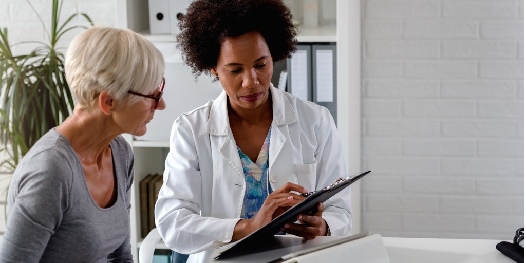 female-doctor-sits-at-her-desk-and-chats-to-an-elderly-female-patient-picture-id1211390857